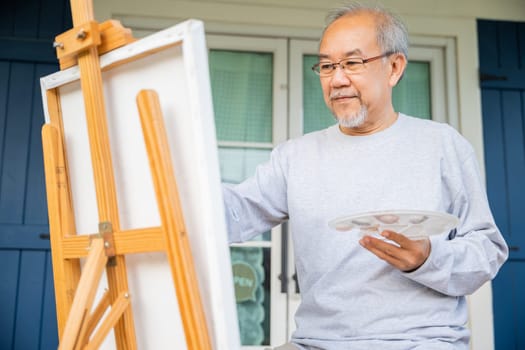 Lifestyle elderly people smile paint at his easel outside home, Asian senior old man painting picture using brush and oil color on canvas, Happy retirement artist and activity concept