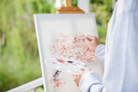 Lifestyle artist. Senior old man painting picture artwork using brush and water color on canvas, portrait elderly white haired paint at his easel outside green nature, Happy retirement and activity