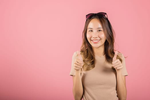 Portrait Asian beautiful young woman smiling she standing made finger thumbs up, Ok sign to agree studio shot isolated on pink background, Thai female successful like finger gesture with copy space