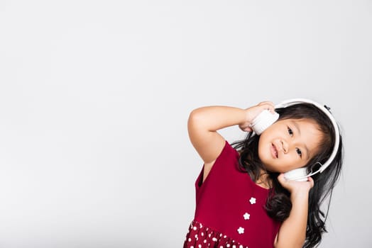 Little cute kid girl 3-4 years old listen music in wireless headphones in studio shot isolated on white background, happy Asian children smiling listening audio, entertainment lifestyle