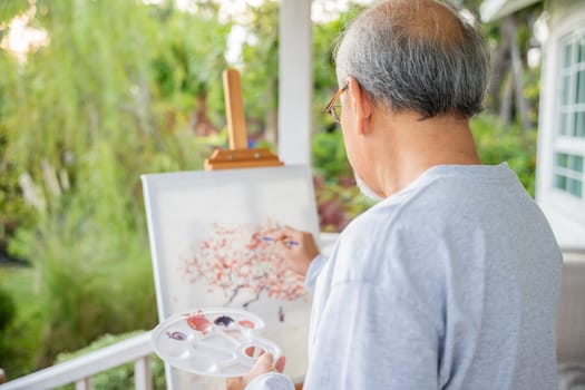 Lifestyle Asian senior old man painting picture artwork using brush and oil color on canvas, elderly people smile paint at his easel outside green nature background, Happy retirement artist activity