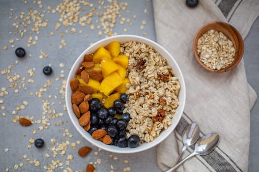 Oatmeal porridge with blueberries, mango and almonds in bowl on concrete grey table from above. flatlay. Healthy breakfast food. Copy space