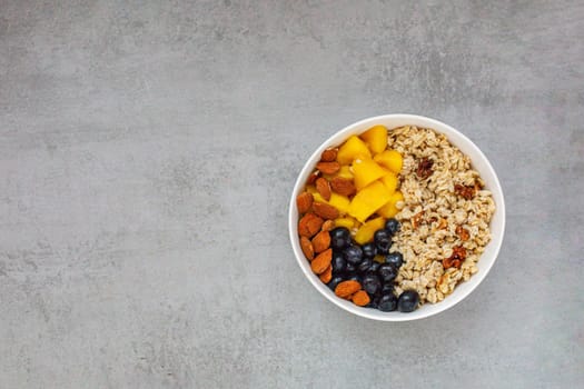 Oatmeal porridge with blueberries, mango and almonds in bowl on concrete grey table from above. flatlay. Healthy breakfast food. Copy space