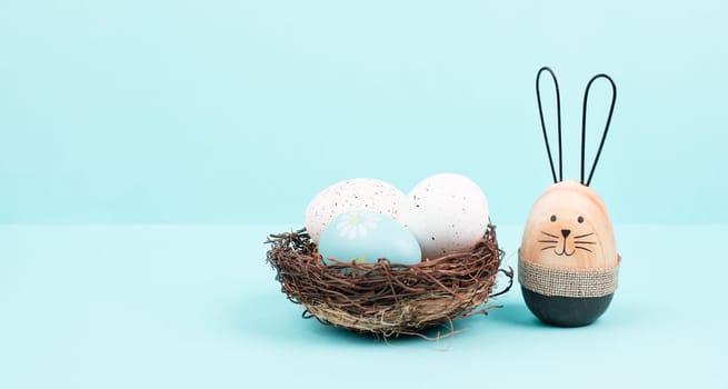 Easter bunny or rabbit sitting nest to a wicker nest filled with colorful eggs, spring holiday