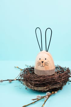 Easter bunny or rabbit sitting in a bird nest, willow branches, wooden egg, spring holiday, brown and blue color