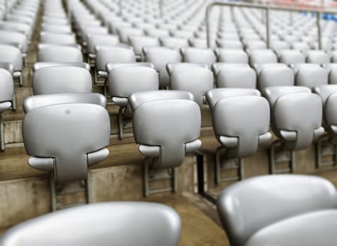 Empty gray chairs inside a stadium. Plastic seats arranged in rows. Repetition and symmetry.