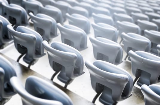 Empty gray chairs inside a stadium. Plastic seats arranged in rows. Repetition and symmetry.