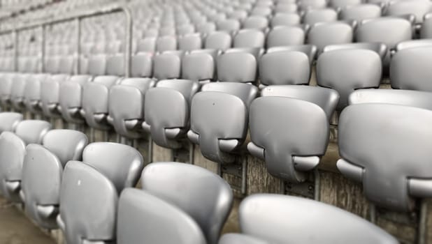 Empty gray chairs inside a stadium. Plastic seats arranged in rows. Repetition and symmetry.