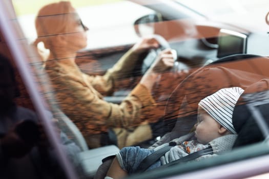 Mother concentrating on driving family car running errands while her baby sleeps in infant car seat by her site