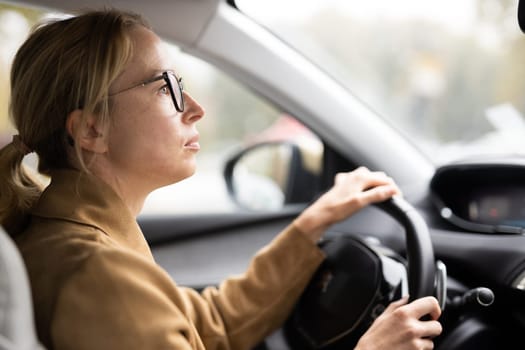Business woman driving a car to work. Female driver steering car on the road.