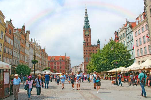 Rainbow in tourist center of Gdansk. Rainbow in city. European tourists walking along street in Gdansk. People walk along city street with beautiful architecture