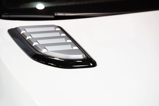 front view closeup detail of sport car with white metal hood and grey air flow intake ornament