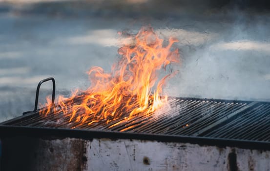 front view of metallic large old barbeque grill with fire flames and smoke coming out
