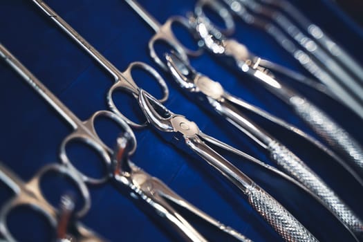 perspective view closeup of row of various steel chrome dental tools on display on blue background with shallow depth of field