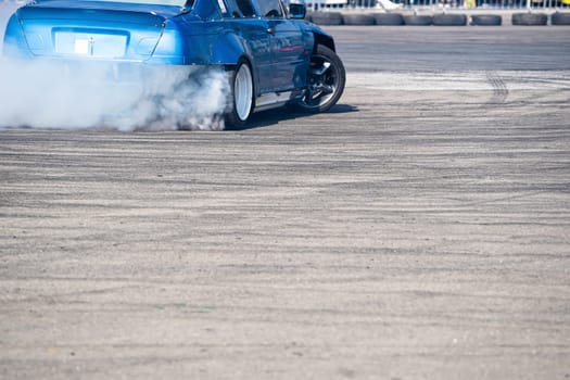 closeup rear view of blue sport car drifting on gray speed tarmac track with white smoke coming out of the back tire wheel with copy space available