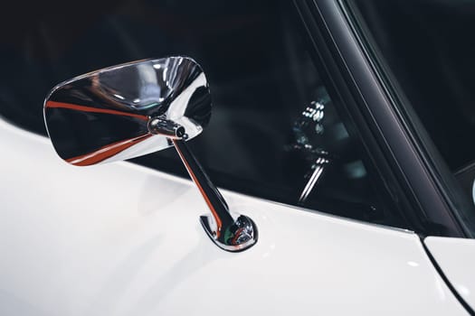 side view detail closeup of chrome rear mirror on white car with classic vintage design