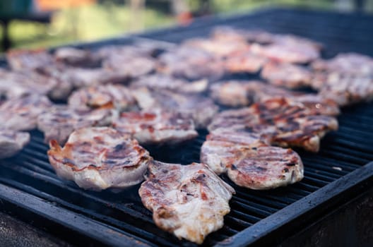 perspective view closeup of pork slices being grilled on black iron barbeque grate outdoors