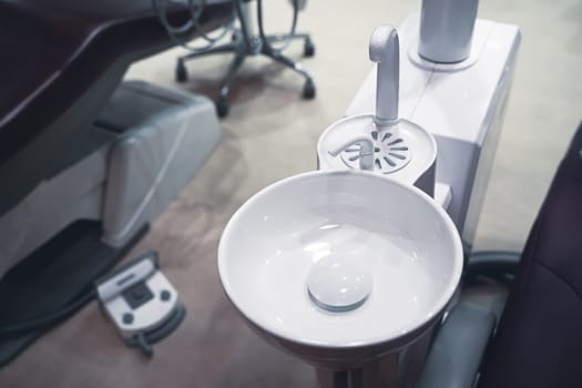 closeup top view of clear dental white ceramic spit sink near chair in dentist office