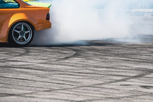 closeup side view of yellow sport car drifting on gray speed tarmac track with white smoke coming out of the back tire wheel with copy space available