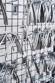 perspective view closeup of row of various stainless steel dental extraction forceps tools hanging on display