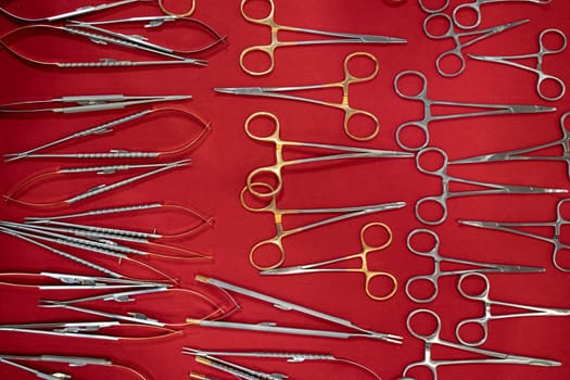 top view closeup of row of medical scissors and other basic stainless steel dental tools supplies on red fabric background