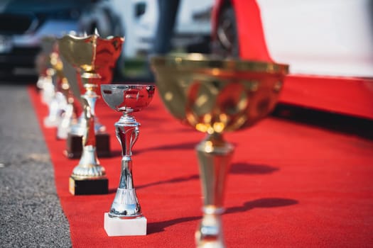 close up perspective view of golden and silver trophy standing  on display on a red carpet with racing cars in the background
