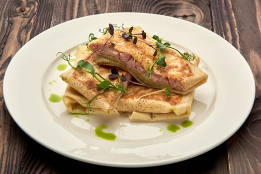 Delicious juicy pancakes with ham on a white plate. High quality photo