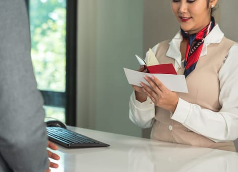 Female flight attendant checking passport and boarding pass at airport terminal counter. Ground staff at departure gate checking travel documents of male passenger