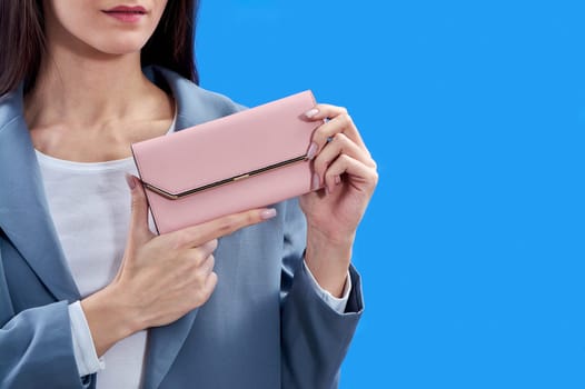 A beautiful young woman is holding a pink purse on a blue background, copy space. High quality photo