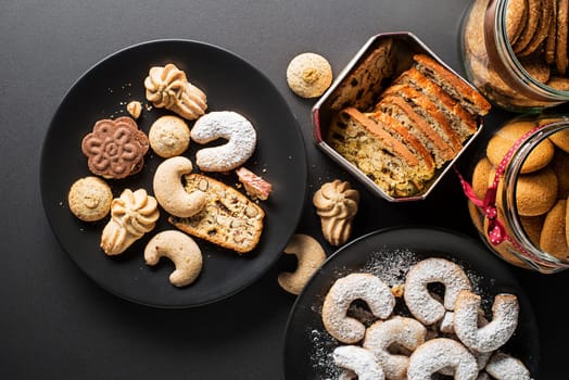Tasty homemade sugar cookies and biscuits of all shapes and sizes on black table background