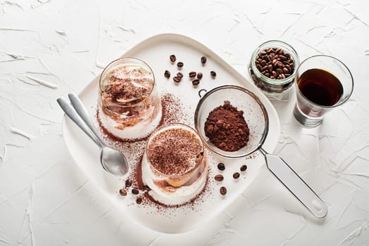Traditional Italian dessert tiramisu in a glass cup. Homemade tiramisu in glass jars, step by step cooking process. Traditional unbaked italian dessert on white background. Coffee and mascarpone cream cake.