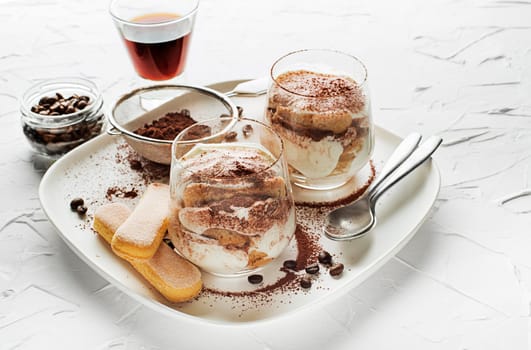 Traditional Italian dessert tiramisu in a glass cup. Homemade tiramisu in glass jars, step by step cooking process. Traditional unbaked italian dessert on white background. Coffee and mascarpone cream cake.