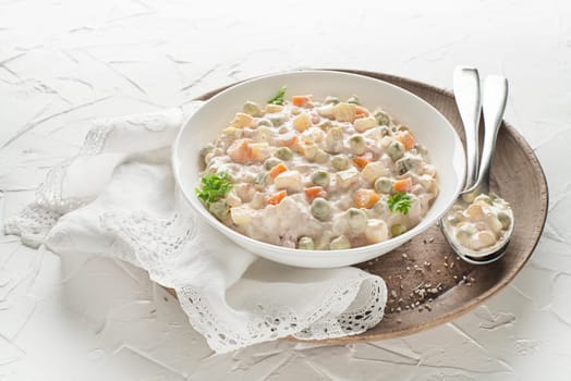 Bowl of russian salad olivier french salad with vegetables and egg dressed with mayonnaise on white table