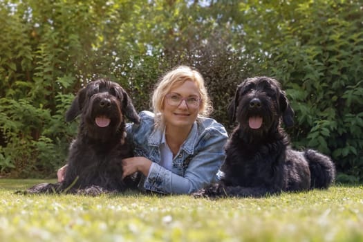 Woman is posing with her two Big Schnauzer dogs outdoors. They are looking at the camera.
