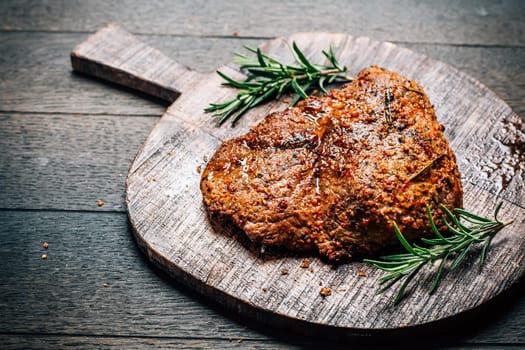 Grilled beef steak with spices on cutting board on wooden background