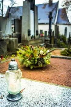 Candle lantern at grave in cemetery. Grief and paying respect for dead person. Tombstones and a chapel in the public cemetery