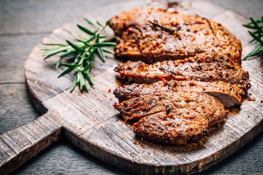 Grilled beef steak with spices on cutting board on wooden background