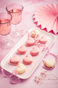 Happy Mothers Day, Happy Valentine - sweet macarons in heart shape and glasses of rose sparkling wine in pink tone