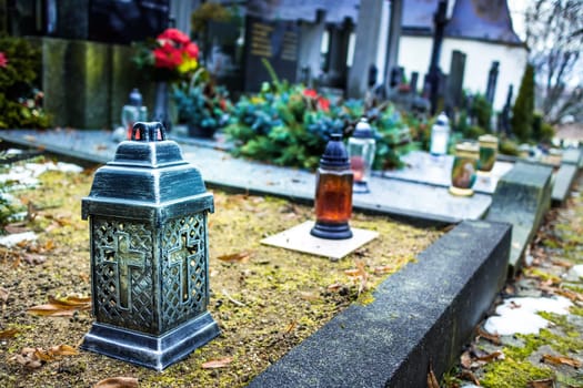 Candle lantern at grave in cemetery. Grief and paying respect for dead person. Tombstones and a chapel in the public cemetery