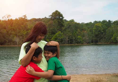 Happy family spending time outdoors hugging and enjoying the view of river. Mother with two kids.