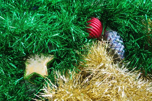 Multi-colored New Year's tinsel and Christmas toys. Green and golden tinsel are intertwined. Christmas decorations. Cone, Christmas ball and star.