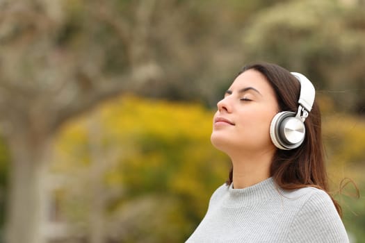 Teen breathing fresh air with headphones meditating in a park