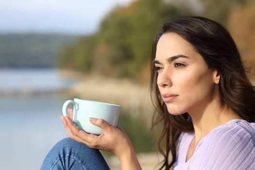 Serious woman drinking coffee looking away sitting in nature