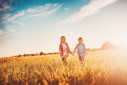 Two children running on the summer field by holding hands. Concept of friendship and family vacation.