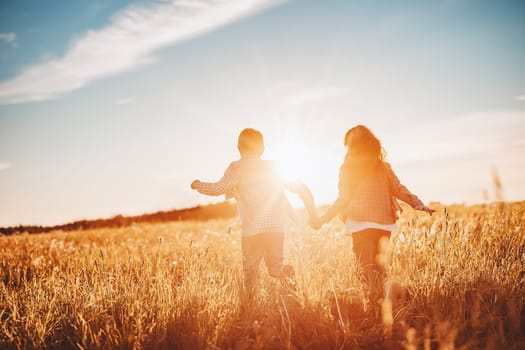 Two children running on the summer field by holding hands. Concept of friendship and family vacation.