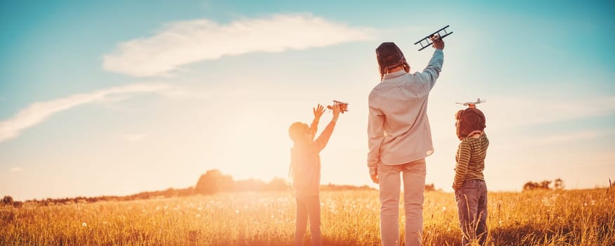Father with his children playing with toy of plane on the evening field. Concept of love and family vacation.