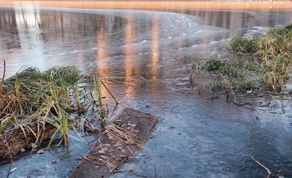 Footbridge in the ice river in early winter. There is some reed on a backgroung of the blue ice with air bubbles. Winter landscape scene