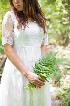 beautiful girl in a white dress holding a fern