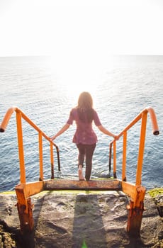 A slender brunette with long hair descends the steps to the sea.