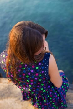 The girl in a beautiful dress is sitting on the pier